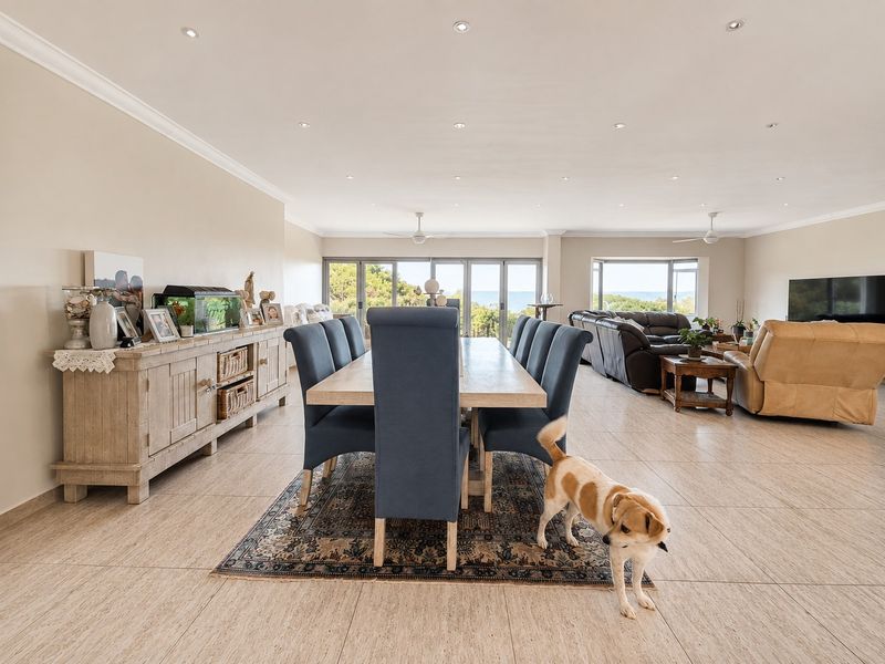 Spacious open-plan living and dining area featuring tiled flooring, recessed lighting, ceiling fans, and large sliding glass doors with ocean views.