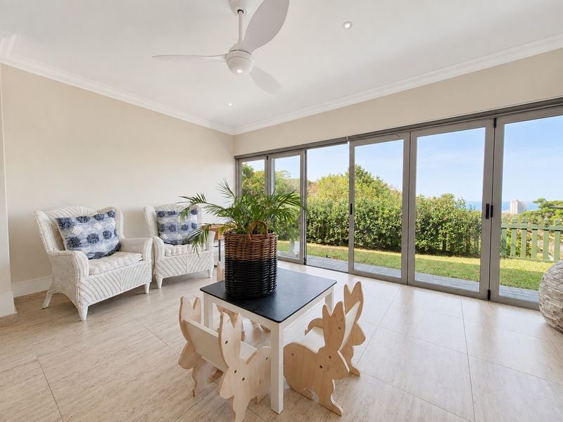 A bright living area featuring large sliding glass doors that open to a garden view, complemented by tiled flooring and a modern ceiling fan.