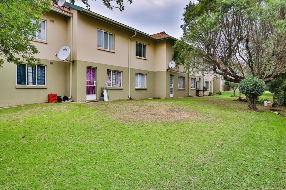 Rear view of the apartment complex featuring a shared garden area, established trees, and exterior access points with security gates.