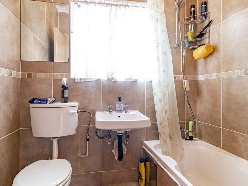 A functional bathroom featuring tiled walls, a wall-mounted basin, a toilet, and a bathtub with a shower attachment.
