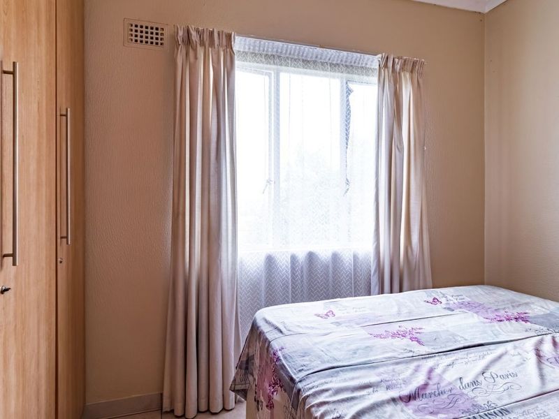 A bedroom featuring a built-in wooden wardrobe and a window with curtains, providing a functional and neutral living space.