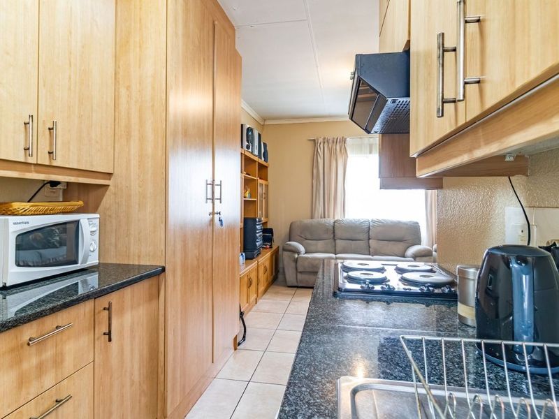 Open-plan kitchen and living area featuring light wood cabinetry, granite countertops, electric hob, and tiled flooring, creating a functional and connected living space.