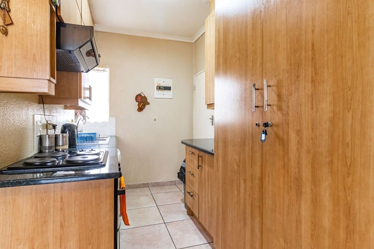 Compact kitchen featuring laminate cabinetry, black granite countertops, an electric hob with extractor fan, and tiled flooring.