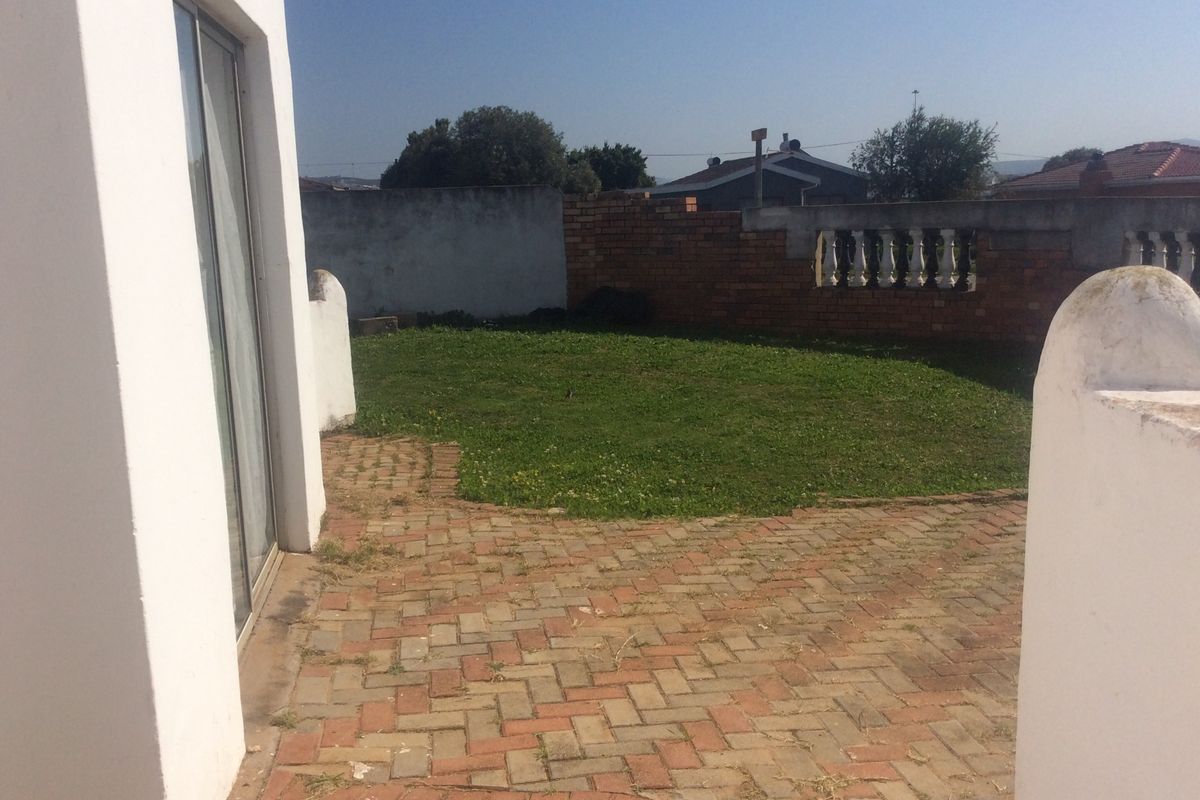 A rear garden area featuring brick paving, a lawn, and a boundary wall with balustrade detailing, accessible via a sliding glass door.