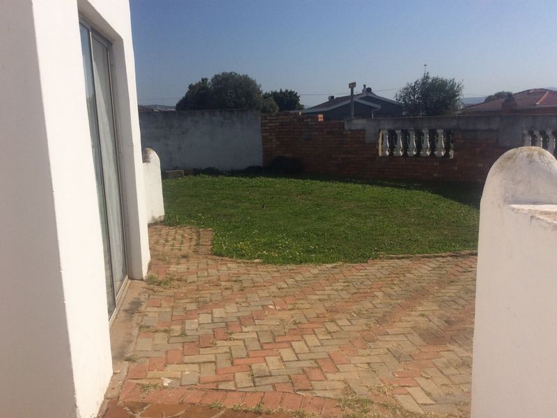 A rear garden area featuring brick paving, a lawn, and a boundary wall with balustrade detailing, accessible via a sliding glass door.