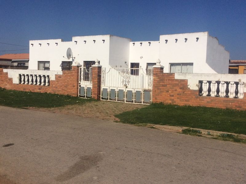 Front elevation of a single-story house featuring a brick boundary wall with concrete balustrades and a metal security gate.