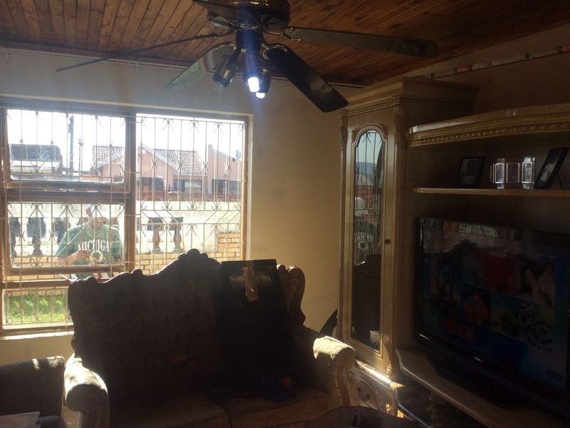 A living room featuring a timber-paneled ceiling, ceiling fan, and security bars on the windows.
