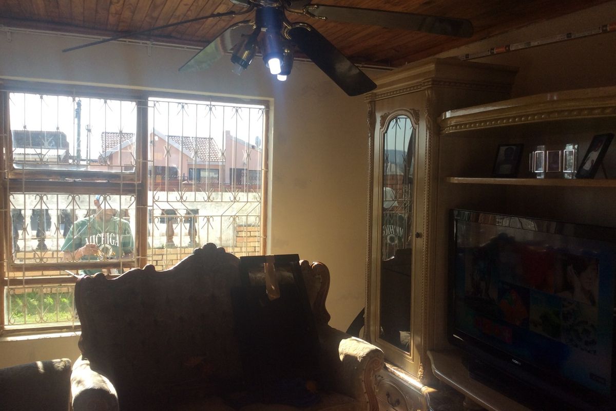 A living room featuring a timber-paneled ceiling, ceiling fan, and security bars on the windows.