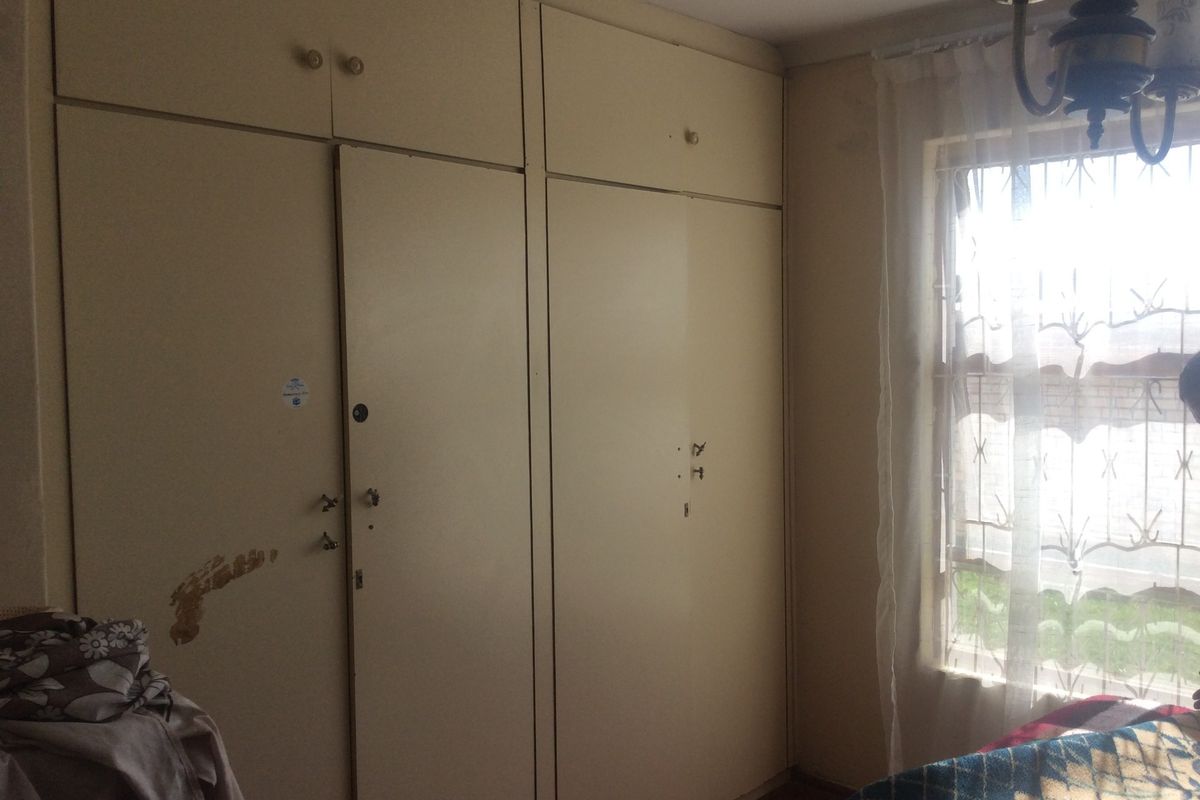 A bedroom featuring built-in cupboards with security bars on the window, requiring cosmetic updates to the cabinetry finish.