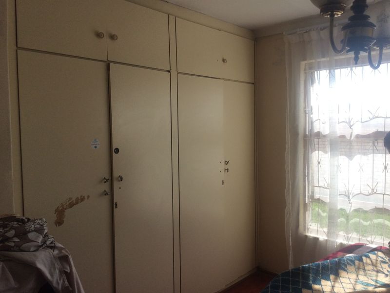 A bedroom featuring built-in cupboards with security bars on the window, requiring cosmetic updates to the cabinetry finish.