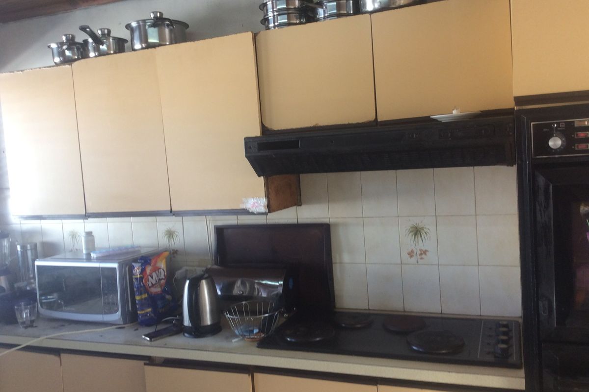A dated kitchen featuring built-in cabinetry, an integrated oven, and an electric hob with a tiled backsplash, requiring cosmetic updates to modernize the space.
