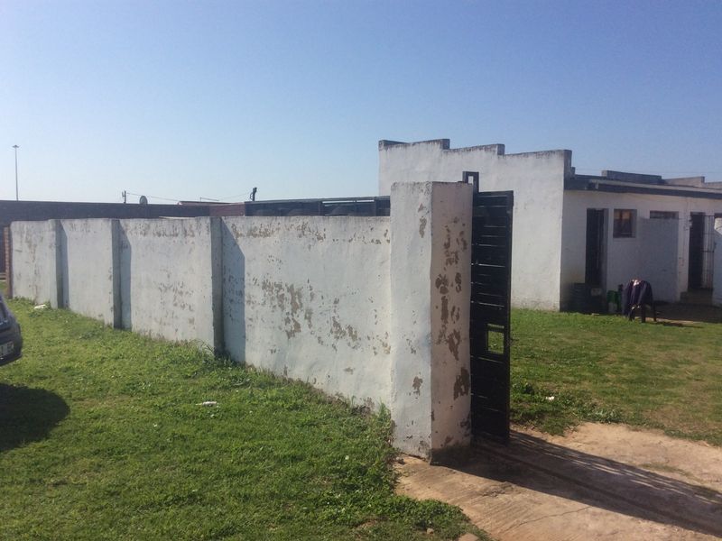 Front exterior view of the property featuring a boundary wall with a metal gate and a grassed yard area.