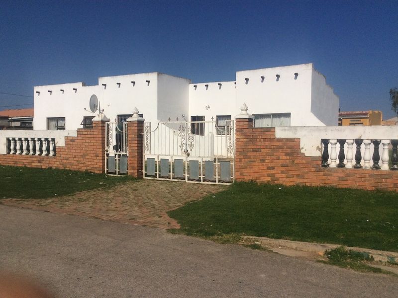 Front elevation of a single-story house featuring a brick boundary wall with concrete balustrades and a metal driveway gate.
