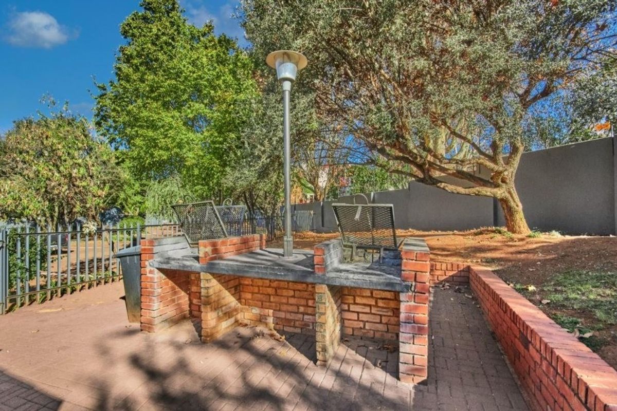 Outdoor communal area featuring a built-in brick braai, paved patio, and perimeter fencing set within a garden space.