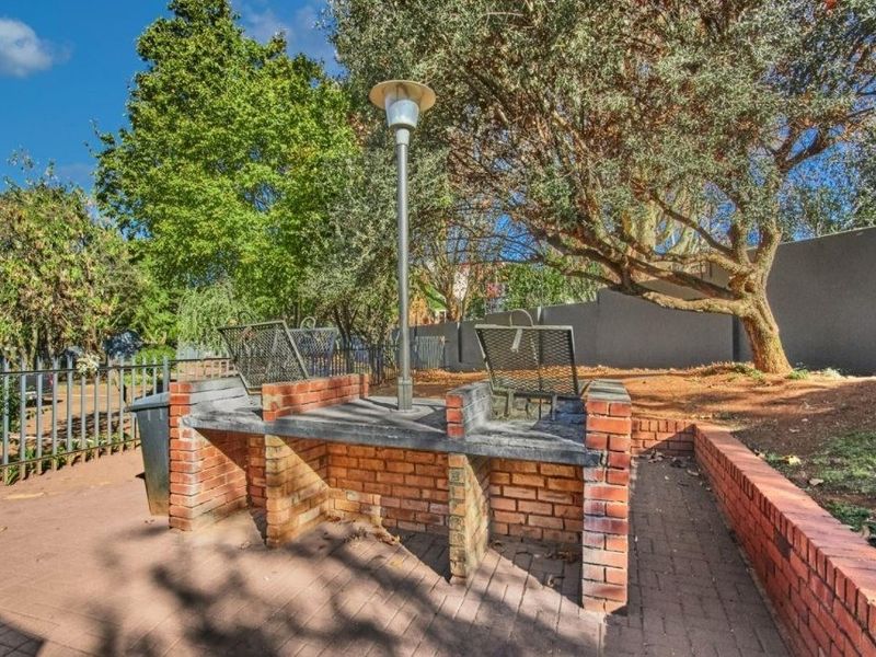 Outdoor communal area featuring a built-in brick braai, paved patio, and perimeter fencing set within a garden space.