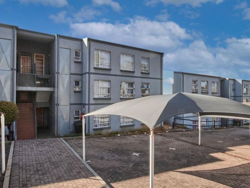 Exterior view of a multi-story apartment complex featuring paved parking areas with shade sail carports and accessible stairwell entrances.