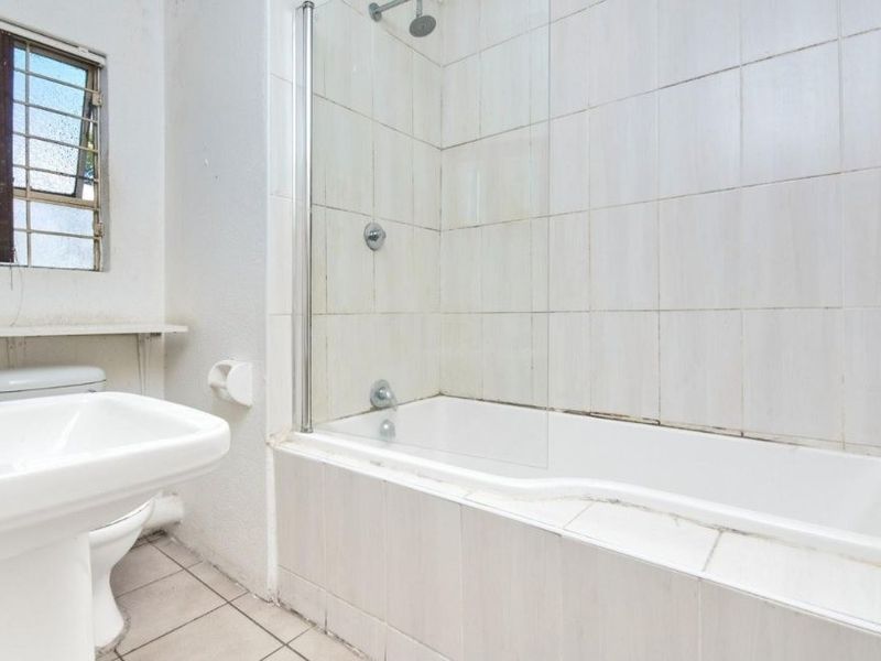 A functional bathroom featuring a pedestal basin, toilet, and a combined bathtub with a glass shower screen and tiled finishes.