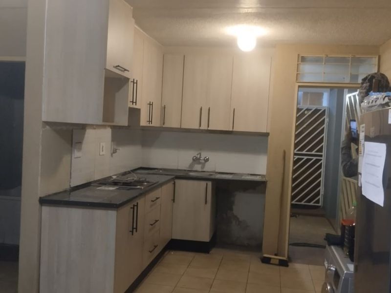 A functional kitchen featuring built-in cabinetry, laminate countertops, and tiled flooring, currently showing signs of wear and requiring minor repairs.