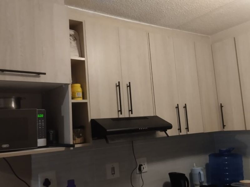 A functional kitchen area featuring light wood-finish cabinetry, a built-in microwave, and an extractor fan above the cooking space.