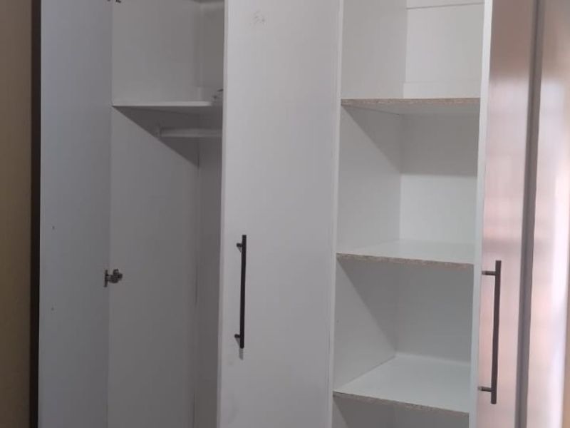 A bedroom featuring a modern white built-in wardrobe with integrated shelving and drawer storage.