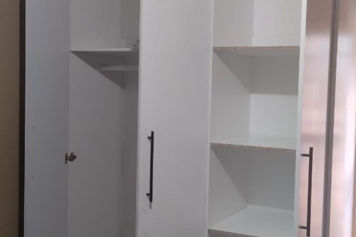 A bedroom featuring a modern white built-in wardrobe with integrated shelving and drawer storage.
