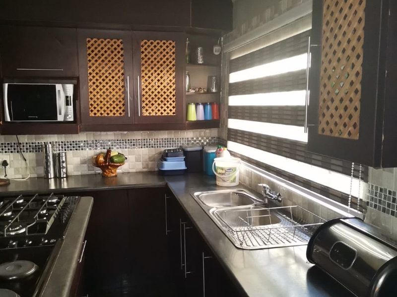 A functional kitchen featuring dark cabinetry, a gas hob, double sink, and mosaic tile backsplash with integrated microwave and roller blinds.