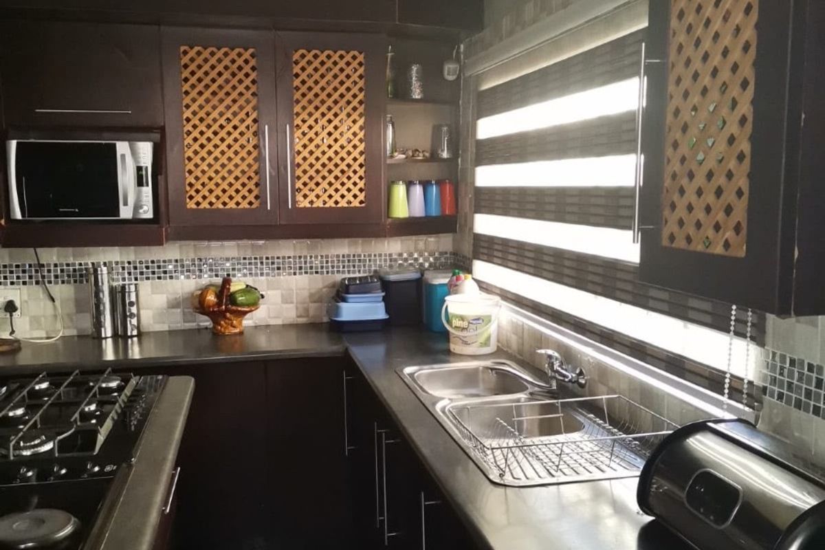 A functional kitchen featuring dark cabinetry, a gas hob, double sink, and mosaic tile backsplash with integrated microwave and roller blinds.