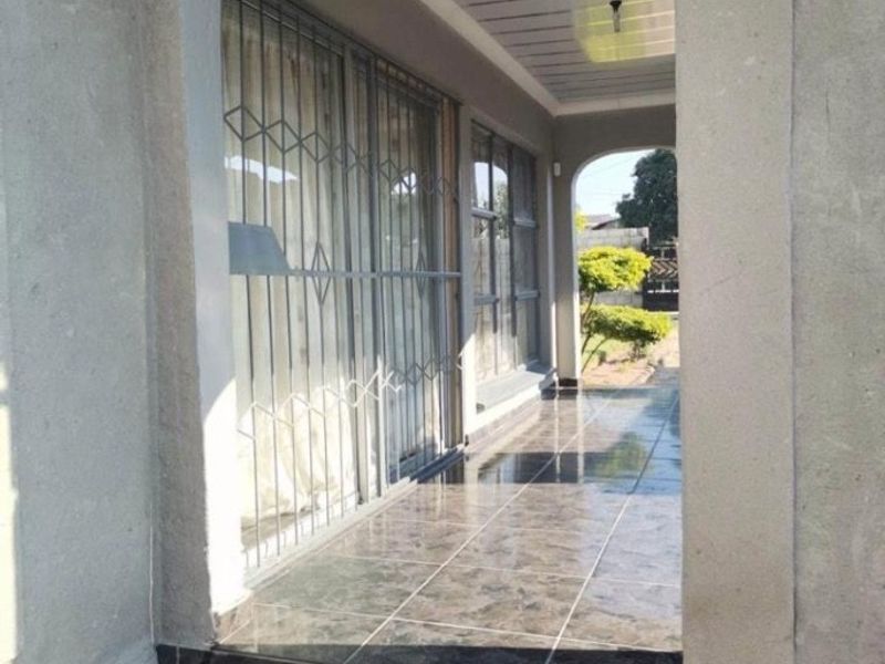 A covered patio area featuring dark tiled flooring, an arched entrance, and security gates over sliding glass doors.