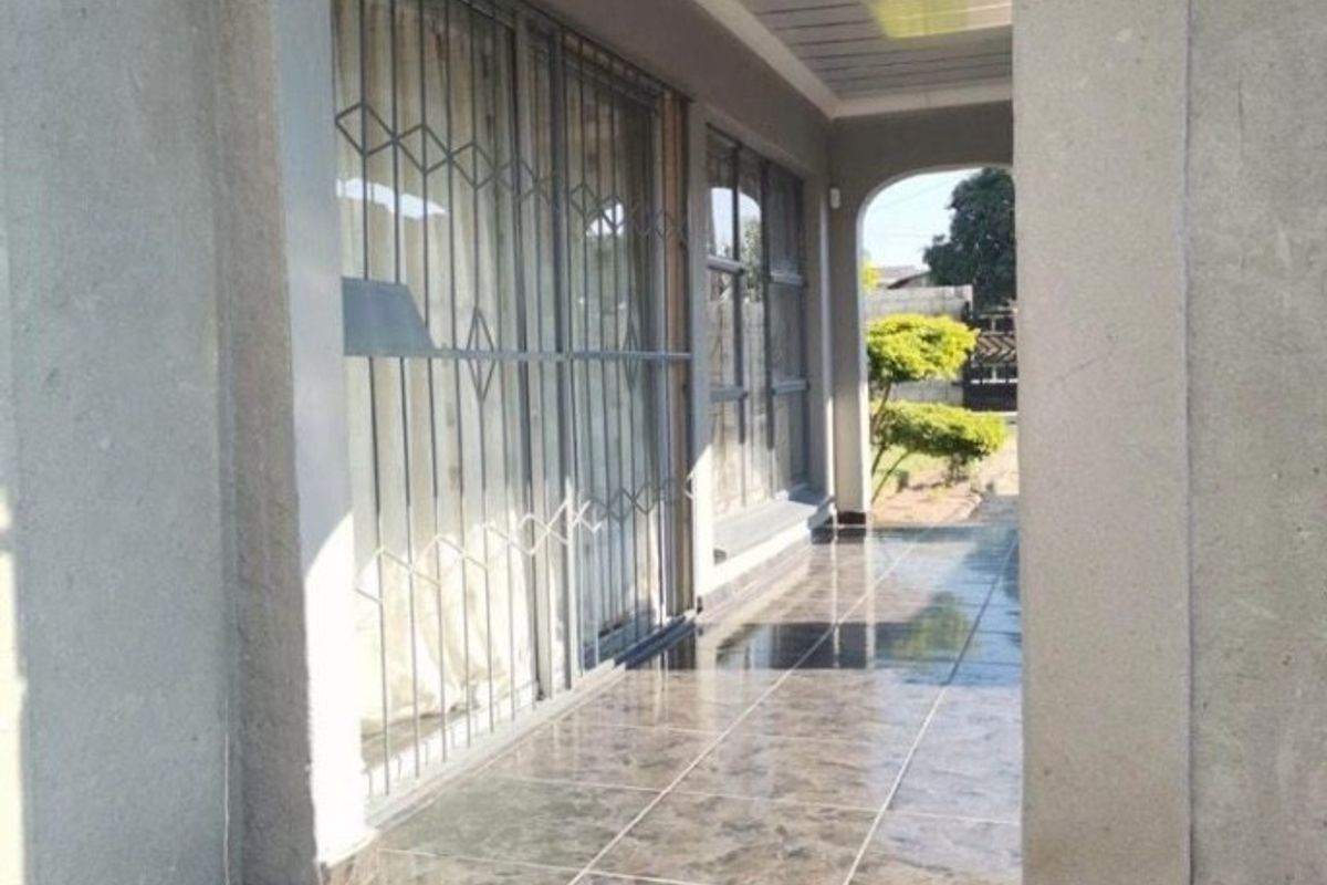 A covered patio area featuring dark tiled flooring, an arched entrance, and security gates over sliding glass doors.