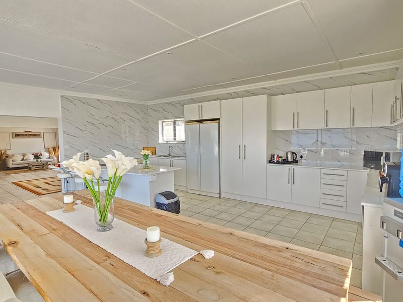 Spacious open-plan kitchen and dining area featuring modern white cabinetry, marble-look splashbacks, and a central island, seamlessly flowing into the adjacent living space.