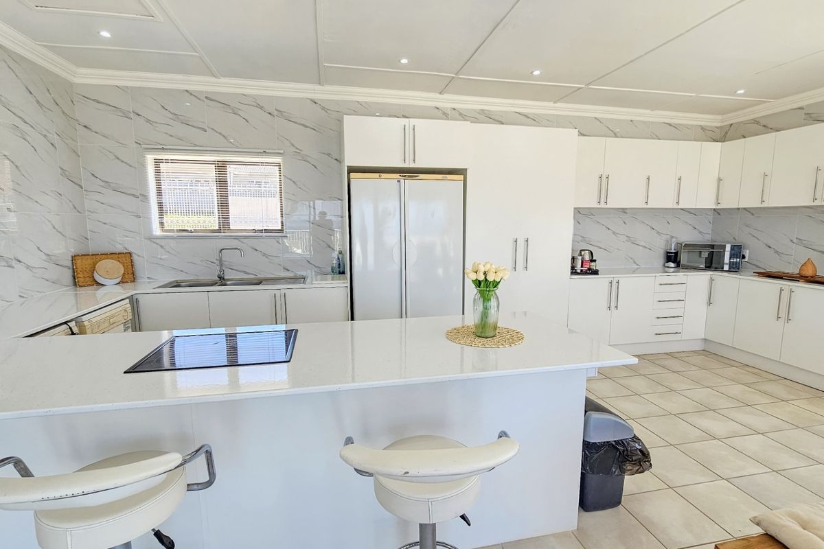 Modern kitchen featuring white cabinetry, marble-look wall tiles, a central island with a quartz countertop, and integrated hob.