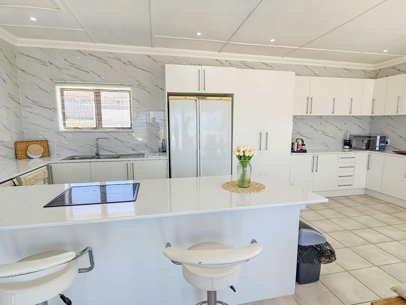 Modern kitchen featuring white cabinetry, marble-look wall tiles, a central island with a quartz countertop, and integrated hob.