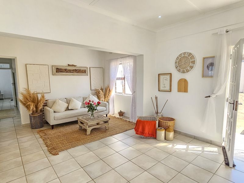 A bright and airy living room featuring neutral tiled flooring, recessed lighting, and direct access to the exterior through a glass-paneled door.