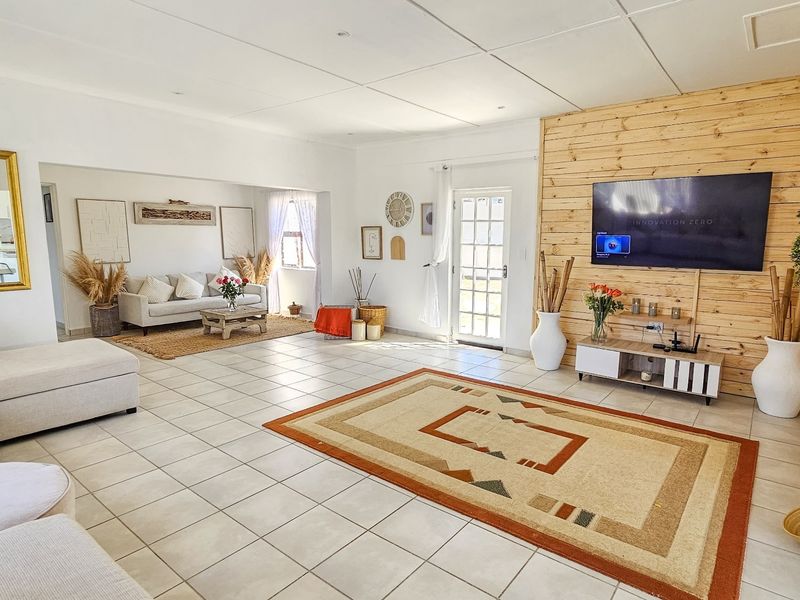 Spacious open-plan living area featuring light-toned tiled flooring, a prominent timber-clad feature wall, and direct access to the exterior via a classic french door.