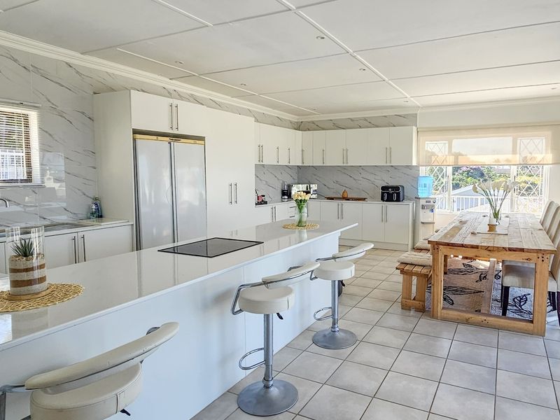 Spacious open-plan kitchen and dining area featuring modern white cabinetry, a large central island with an induction cooktop, and marble-look wall finishes.