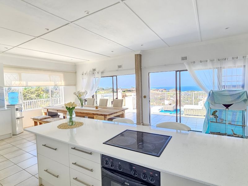 Bright open-plan kitchen and living area featuring a central island with built-in hob, tiled floors, and large sliding doors opening to a scenic balcony.
