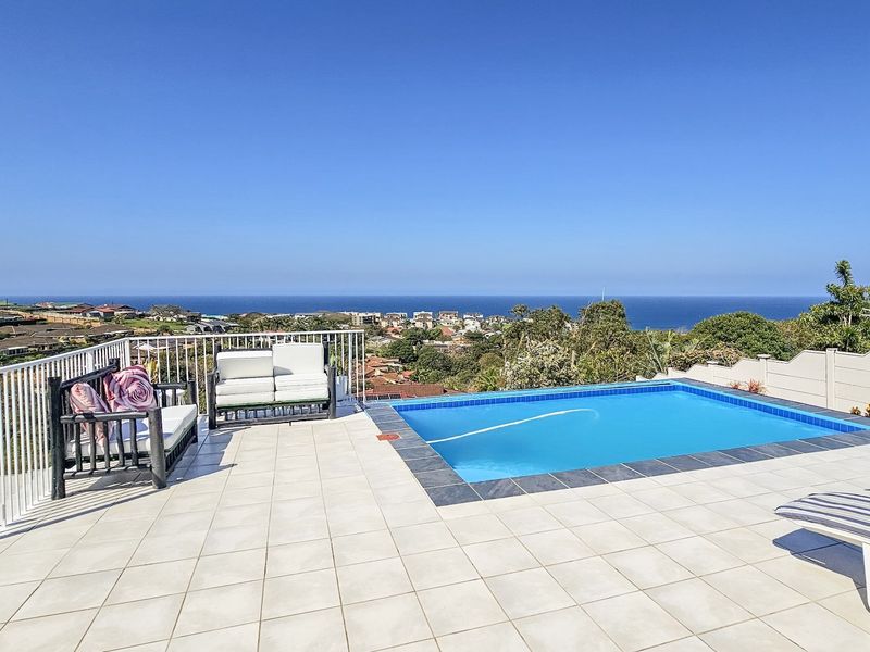 Elevated pool deck featuring a swimming pool with expansive coastal and ocean views, complemented by a tiled patio area and secure metal balustrading.