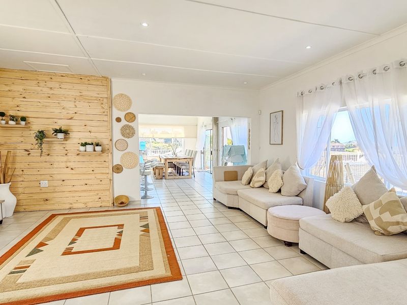 Bright open-plan living area featuring tiled floors, a timber accent wall, and seamless flow to the adjacent dining space and outdoor area.
