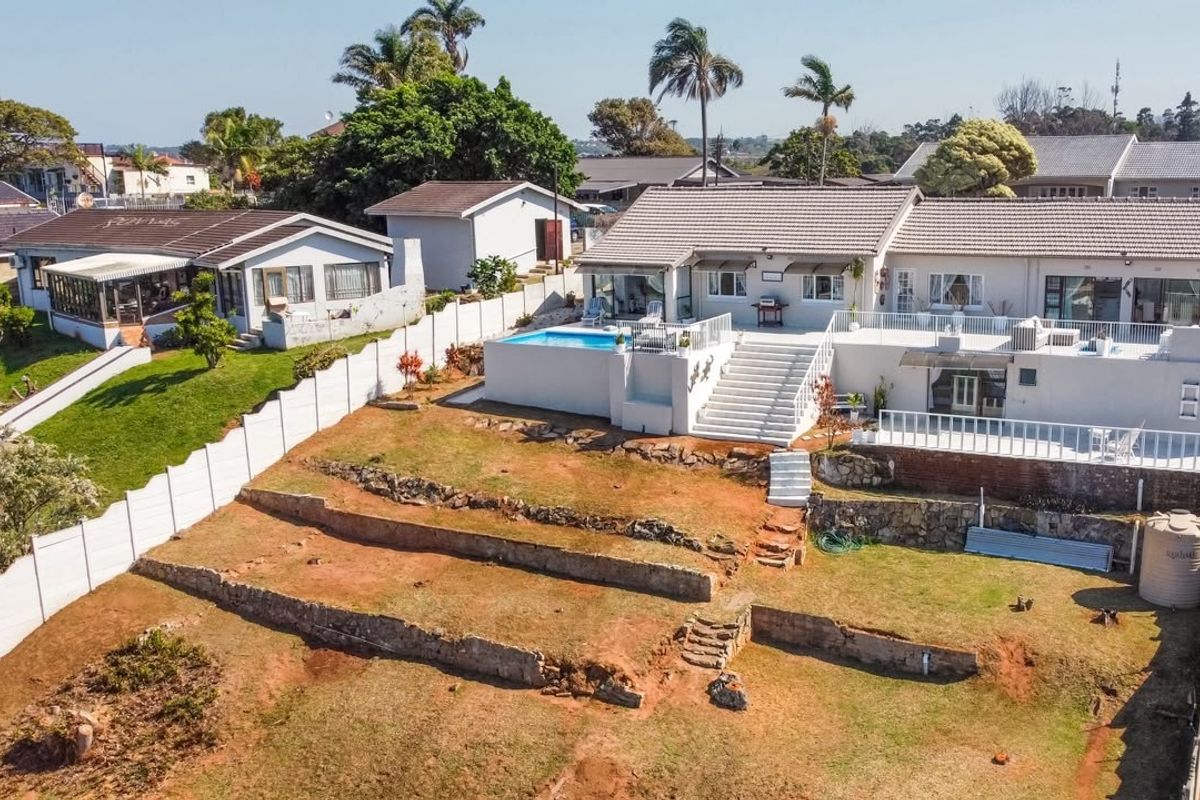 Aerial view of the property featuring a swimming pool, tiered garden with retaining walls, and a spacious rear patio area.