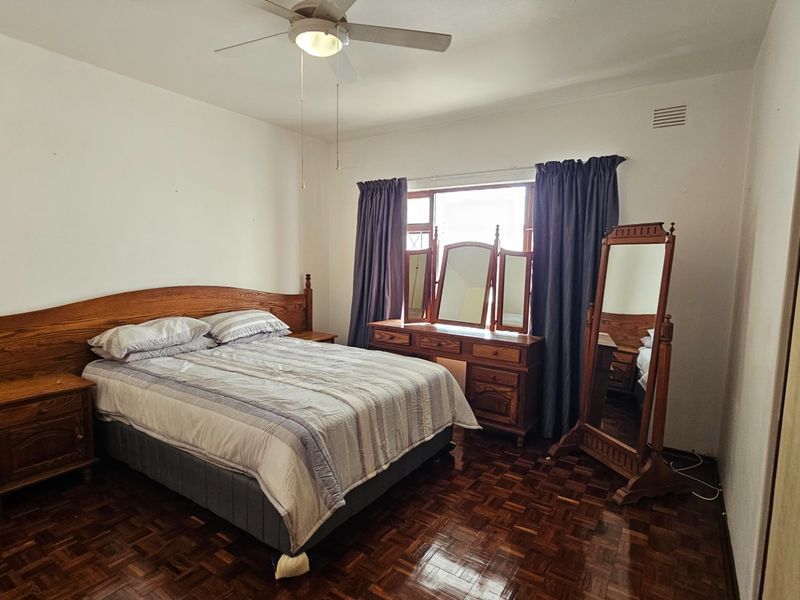 A bedroom featuring classic parquet flooring, a ceiling fan, and built-in wardrobe storage, offering a functional space with traditional finishes.