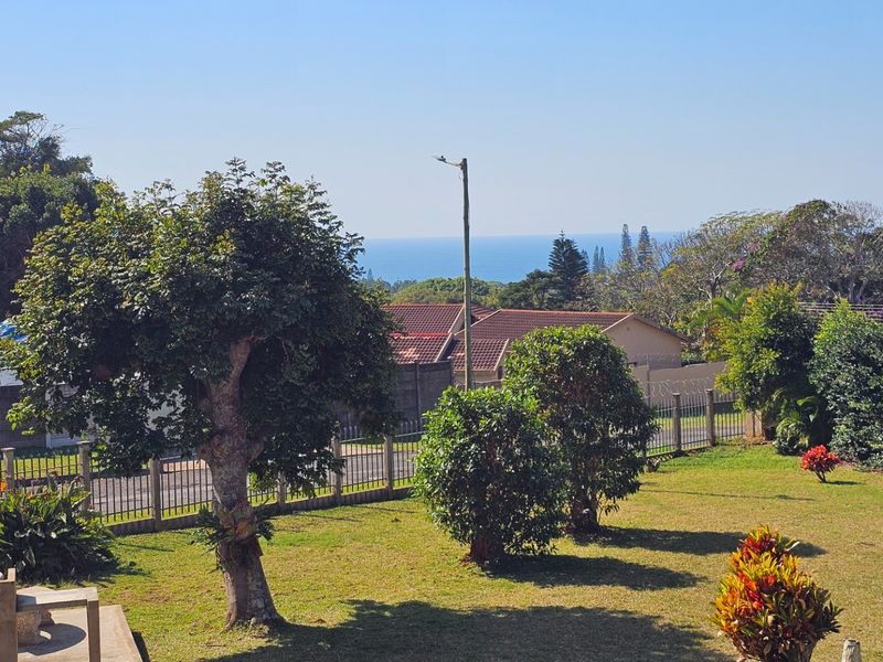 A scenic view overlooking a well-maintained garden with perimeter fencing and distant ocean views.