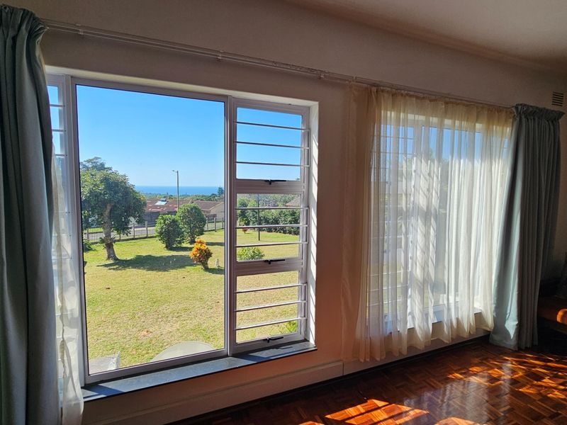 Living room featuring classic parquet flooring and large windows with security bars, offering pleasant views of the surrounding garden and neighborhood.