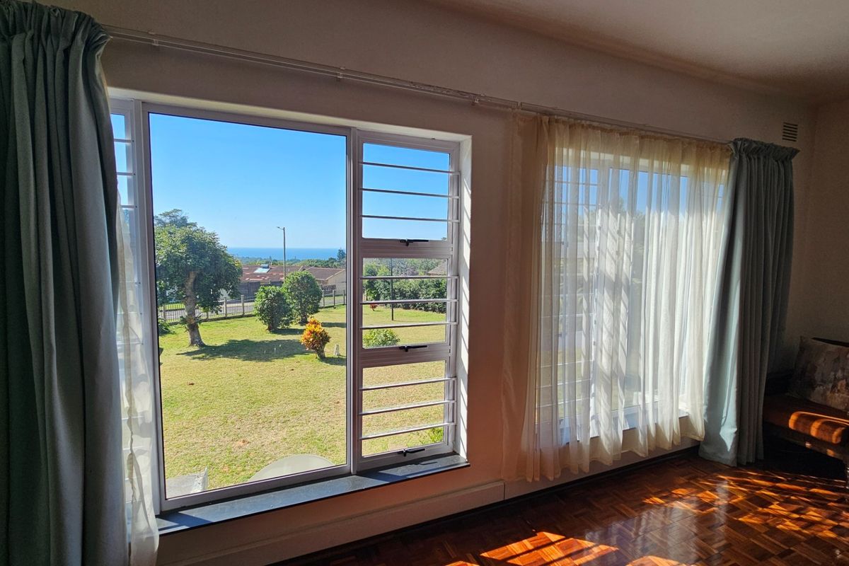 Living room featuring classic parquet flooring and large windows with security bars, offering pleasant views of the surrounding garden and neighborhood.