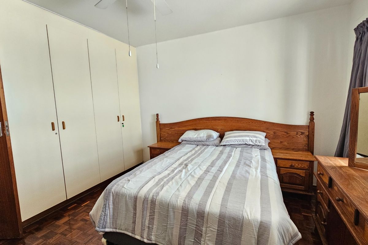 A bedroom featuring parquet flooring, built-in cupboards, and a ceiling fan, offering a functional space with classic finishes.