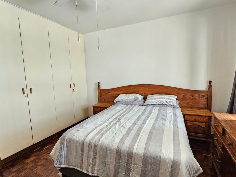 A bedroom featuring parquet flooring, built-in cupboards, and a ceiling fan, offering a functional space with classic finishes.