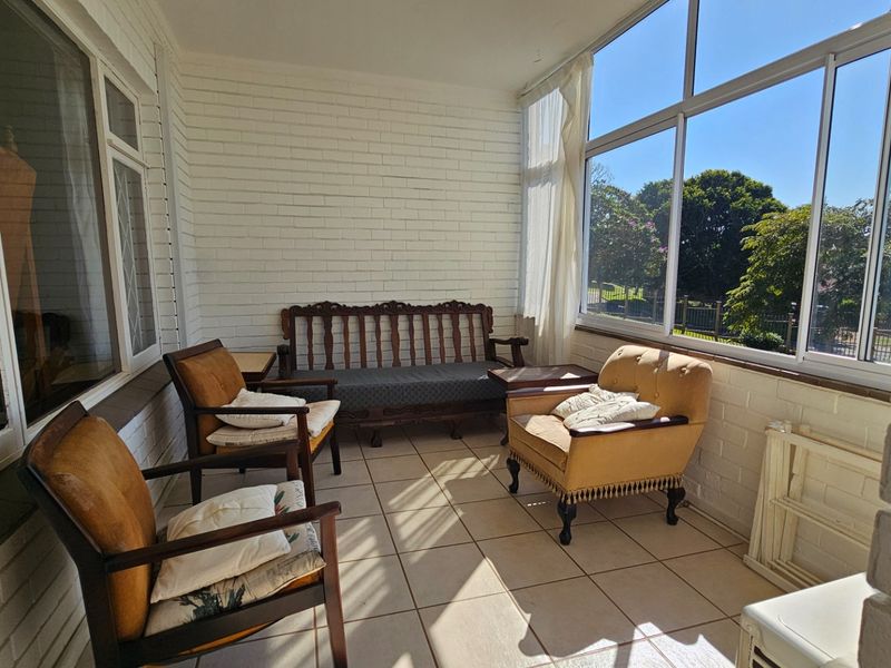 A bright, enclosed patio or sunroom featuring tiled flooring, painted brick walls, and large windows providing natural light and outdoor views.