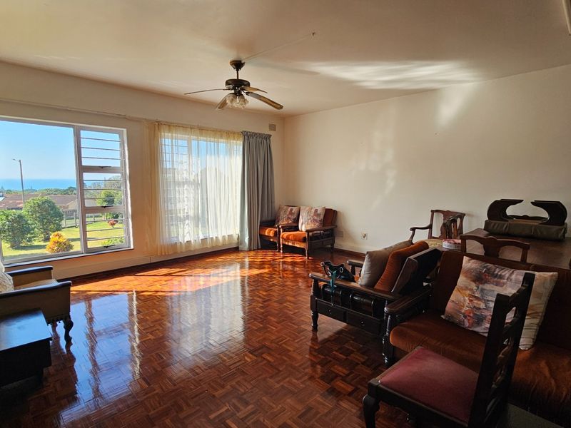 Spacious living room featuring polished parquet flooring, a ceiling fan, and large windows that provide natural light and scenic views.
