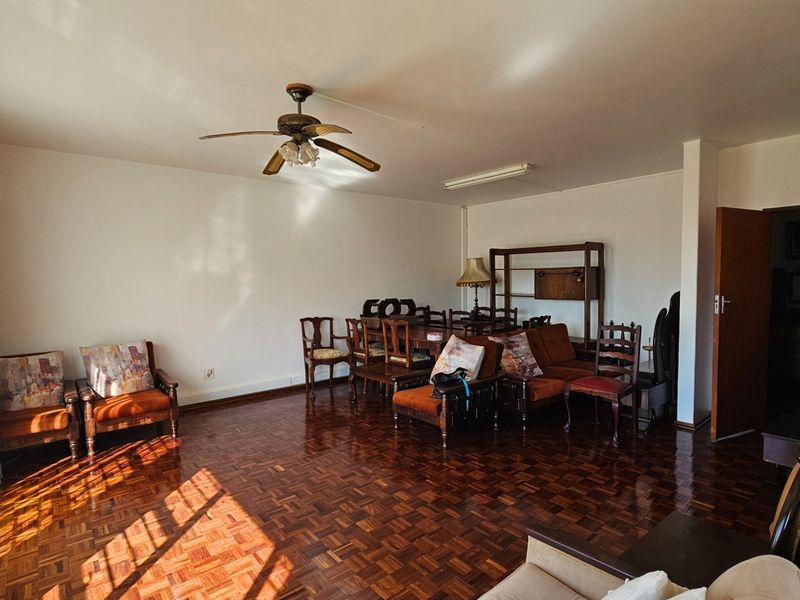 Spacious living area featuring classic parquet flooring, a ceiling fan, and ample natural light from large windows.