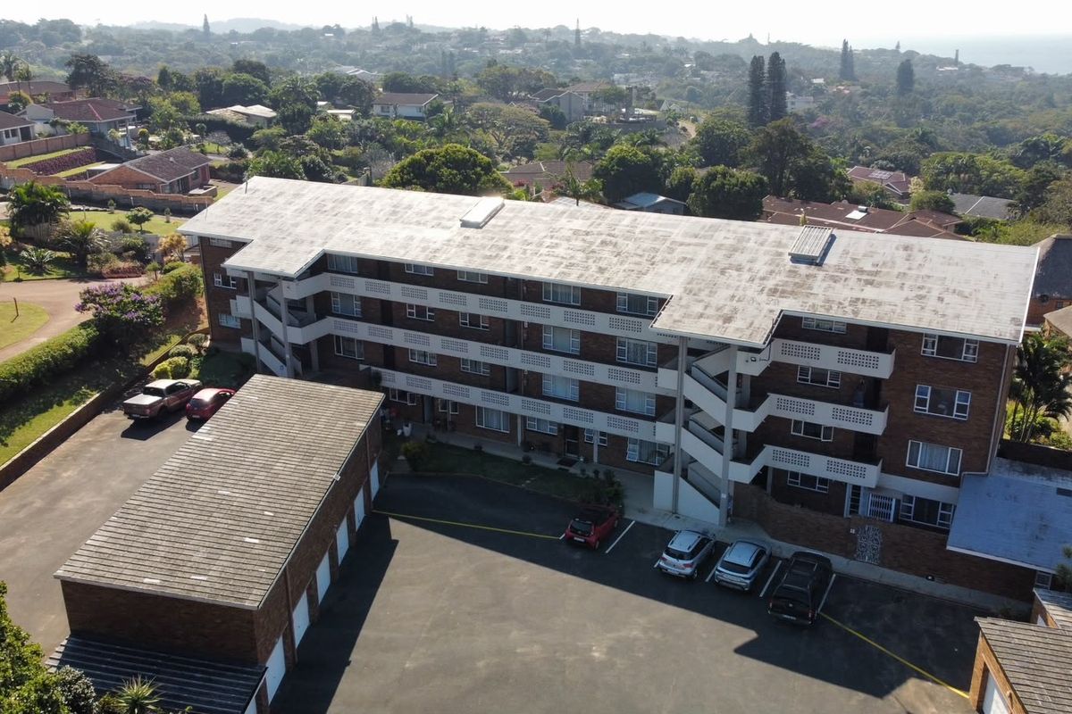 Aerial view of a multi-story brick apartment complex featuring a flat roof, external stairwells, and an adjacent asphalt parking area with garage units.