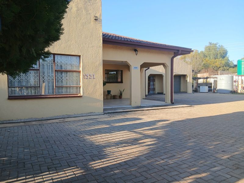 Front elevation of a single-story house featuring a paved driveway, covered patio area, security bars on windows, and an attached garage.